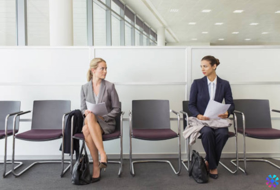 Two businesswomen seated in an office waiting room, discussing the talent market outlook.