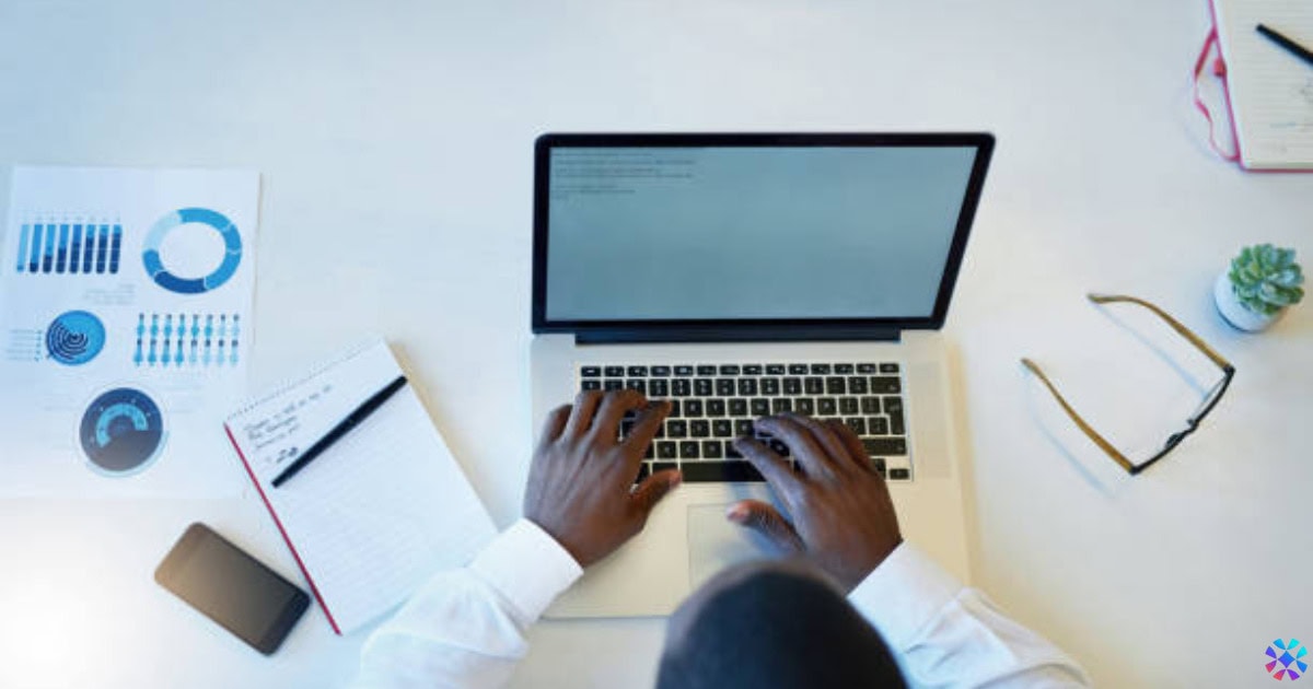 A person typing on a laptop at a desk, focused on creating job descriptions.