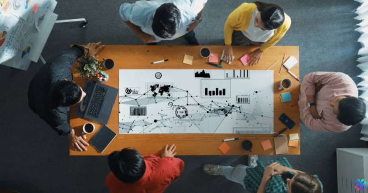 A group of people seated around a table, discussing job descriptions with a whiteboard in the background. Walmart